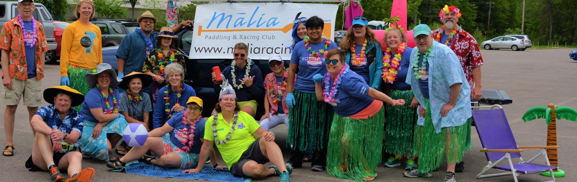 Volunteers dressed in Hawaiian clothes posing in front of Malia poster